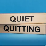 Holzblöcke mit den Worten „Quiet“ und „Quitting“ auf blauem Hintergrund veranschaulichen das Thema Quiet Quitting im Arbeitskontext.